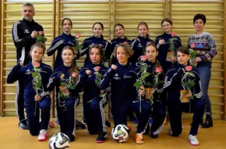 Zdjęcie drużyny sportowej dzieci w nowych strojach wraz z panią Prezes i Wiceprezes Banku oraz trenerem i dyrektorem