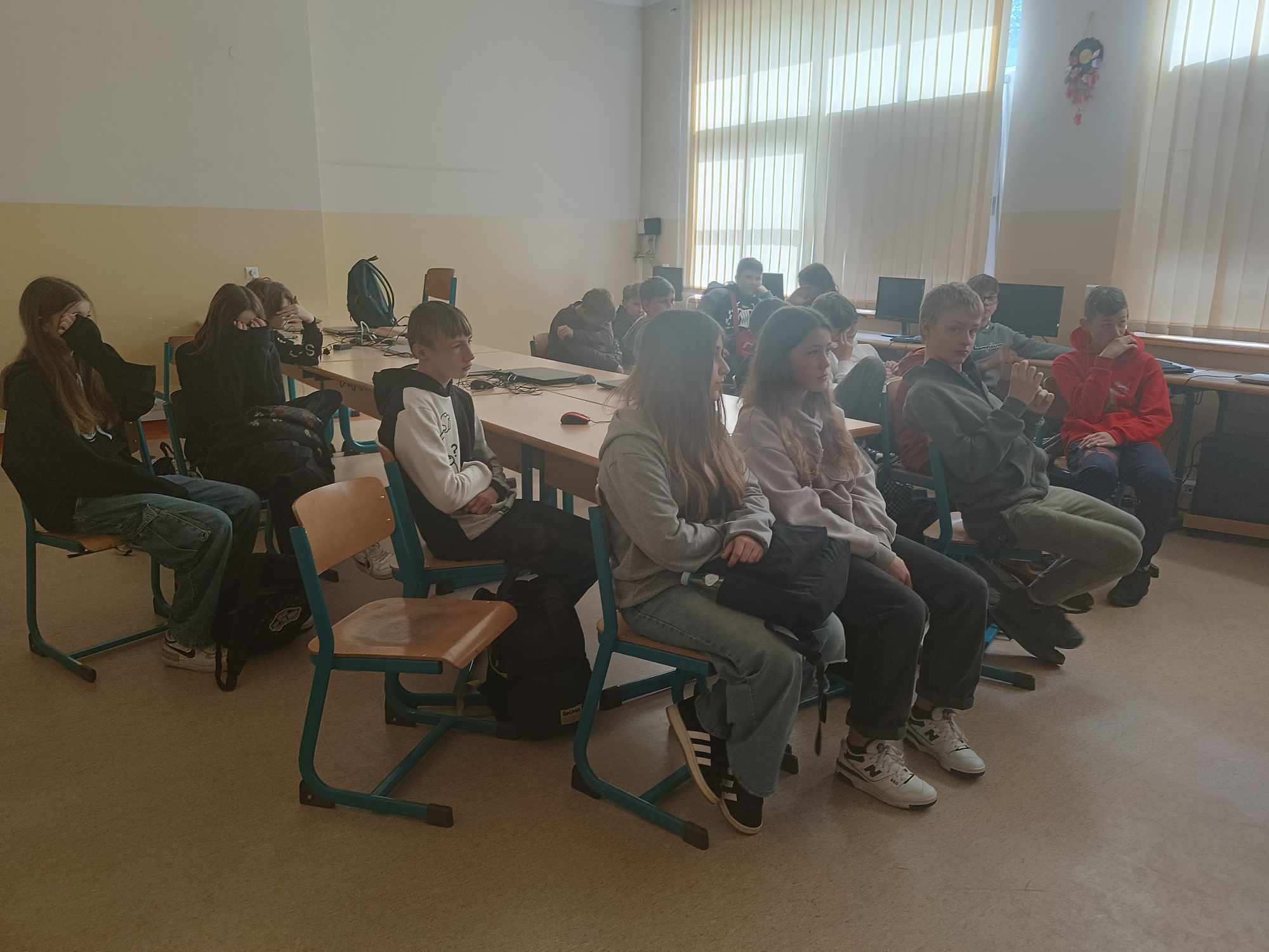 Uczniowie siedzący w pracowni komputerowej, słuchają prezentacji